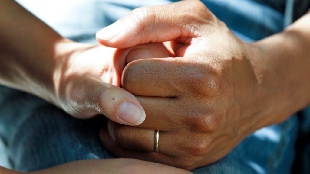Close up of a caregiver holding a senior patient's hand with compassion in a home health setting.